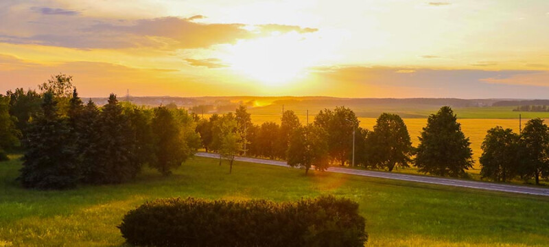 country road sorrounded by trees with sun shining through the clouds  