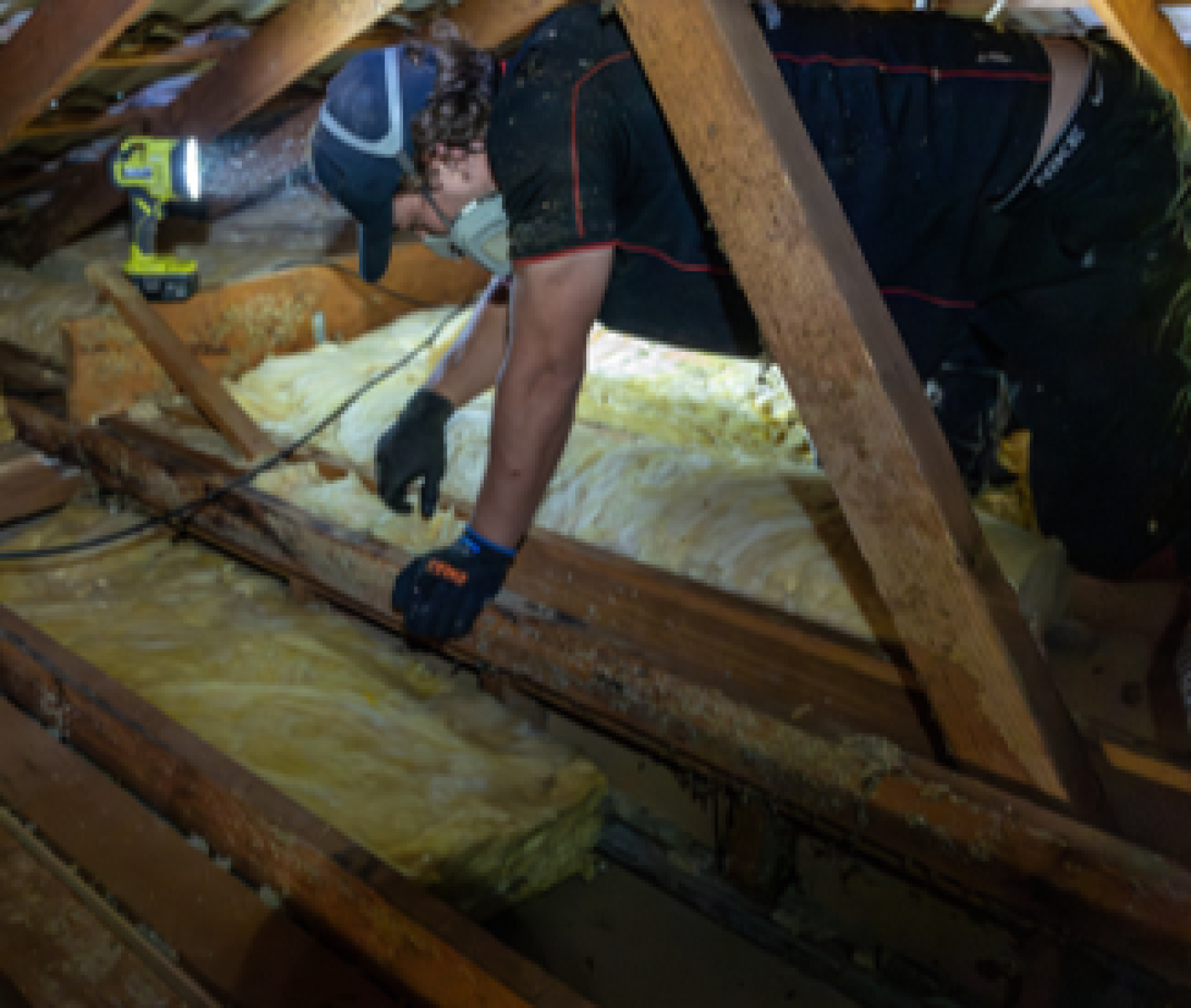 A worker inspecting or installing yellow insulation inside an attic 