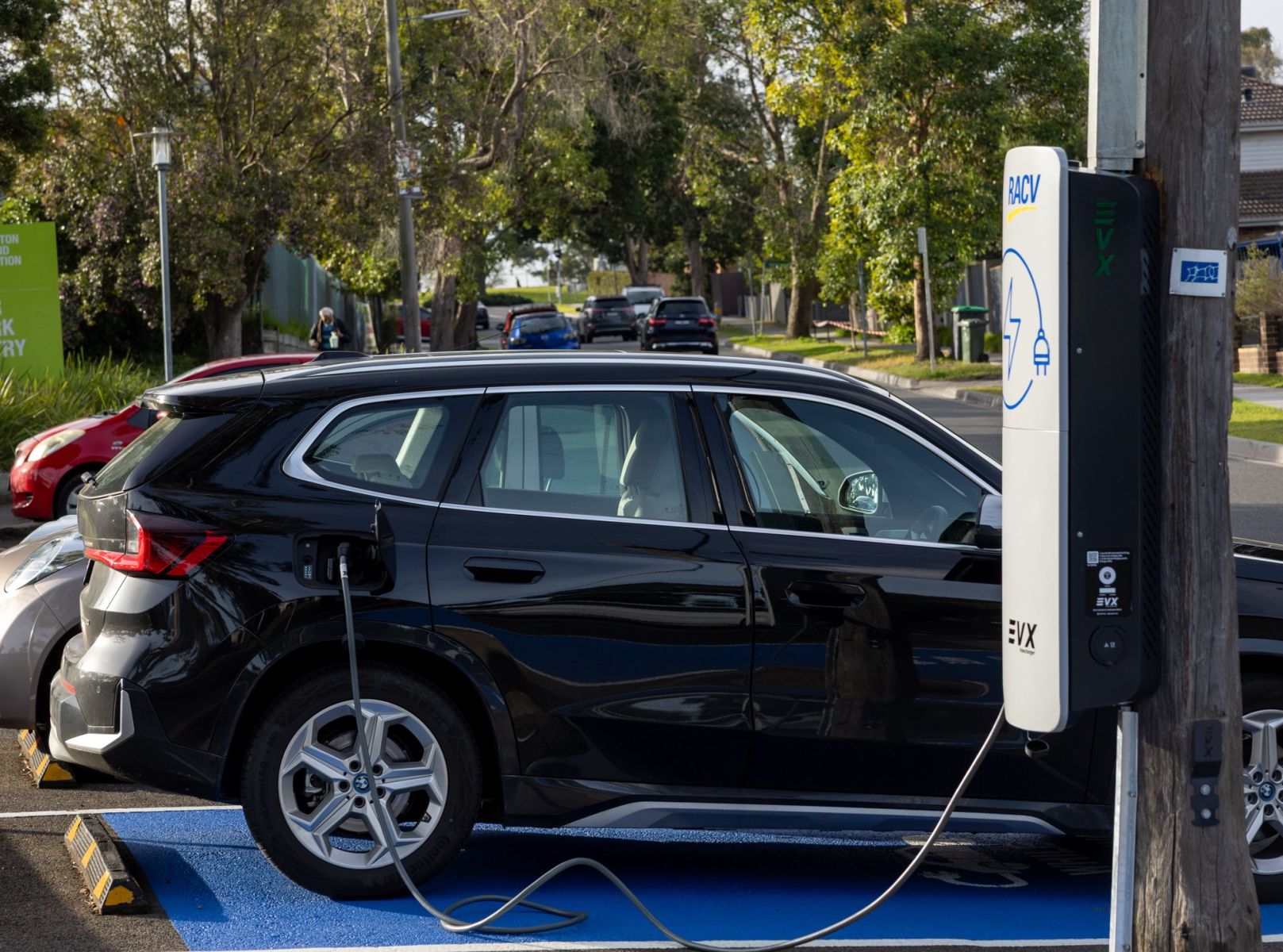 Photo of black car connected to a pole-mounted EV charger in a public carpark. 