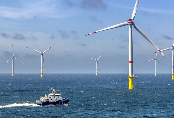 Offhosre wind farm in the ocean with a boat sailing in front