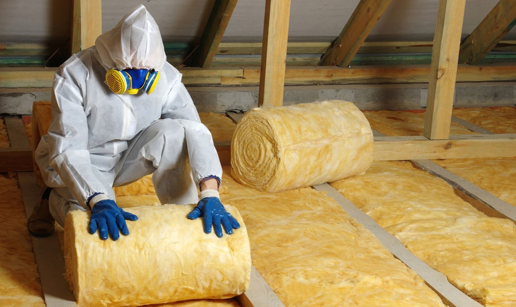 Person in protective clothing rolling out insulation in ceiling