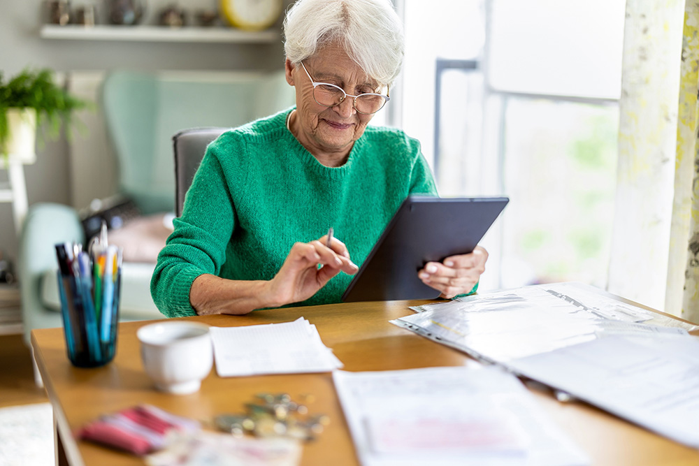 An older female sitting at a table using an ipad