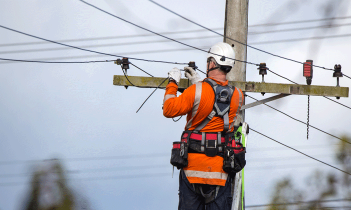 Photograph of a man in safety gear working on overhead powerlines  