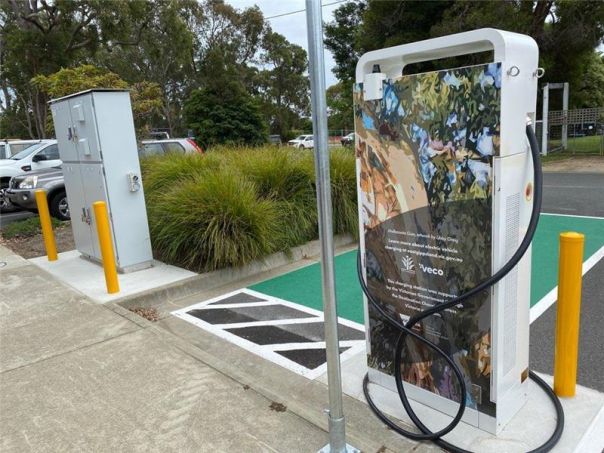 Photo of an electric vehicle charger in a car park. The charger features artwork of a gum tree. 