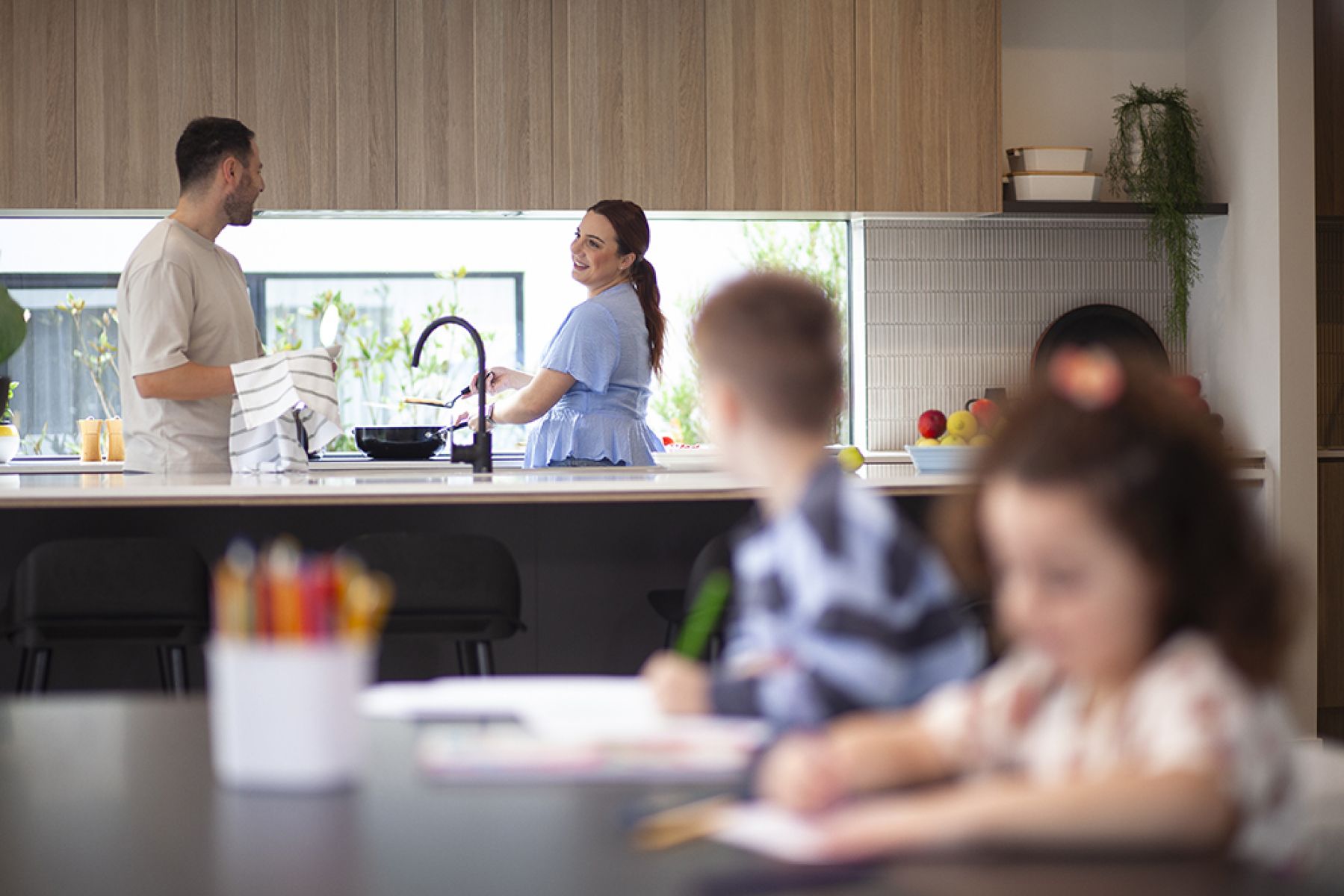 Family in a kitchen with parents at bench cooking and children at table
