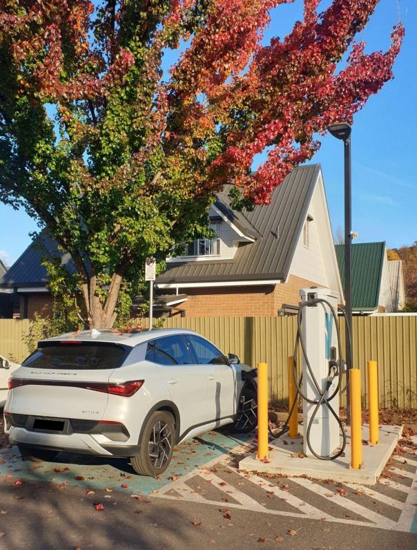 Photo of a white electric vehicle at a charging station with a red autumn tree in background
