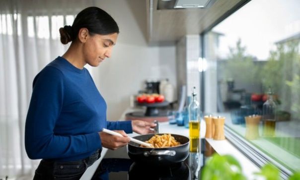 Person cooking pasta in a modern kitchen with large windows showing an outdoor view