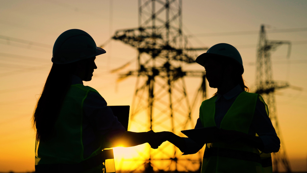 Two people in protective helmets in front of transmission lines  