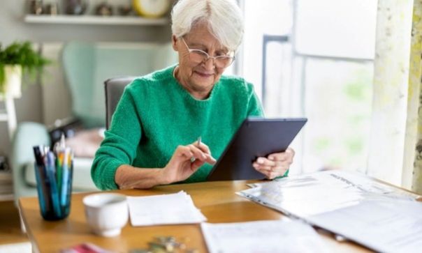 Person wearing glasses and a green sweater using a tablet while sitting at a wooden table