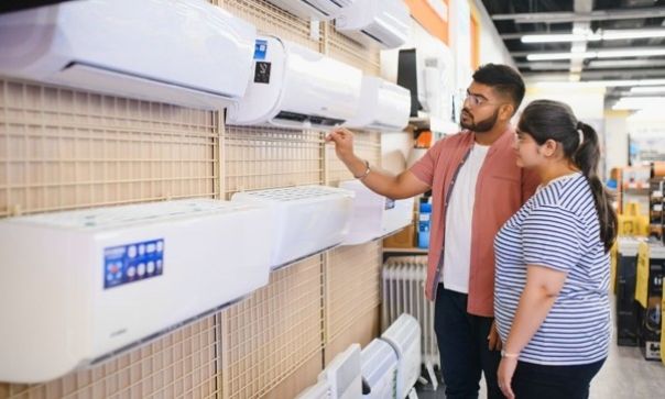 Two people examining wall-mounted air conditioning units in a retail store